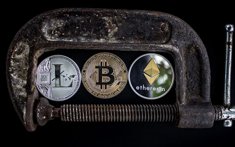 Drei Kryptomünzen in einem Schraubstock eingeklemmt