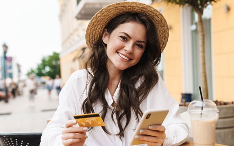Junge Frau mit Smartphone und Debitkarte in einem Café
