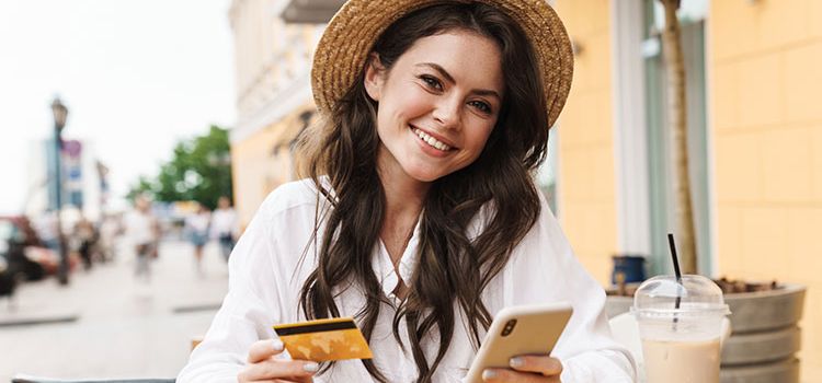 Junge Frau mit Smartphone und Debitkarte in einem Café