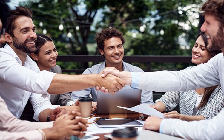 Businessleute an einem Tisch mit Handschlag, als Symbol für Kooperation