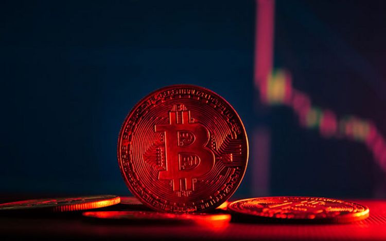 Bitcoin als Münze mit sinkender Kurskurve im Hintergrund