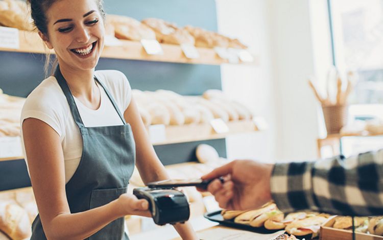 Junge Frau nimmt in der Bäckerei eine Smartphone-Zahlung entgegen