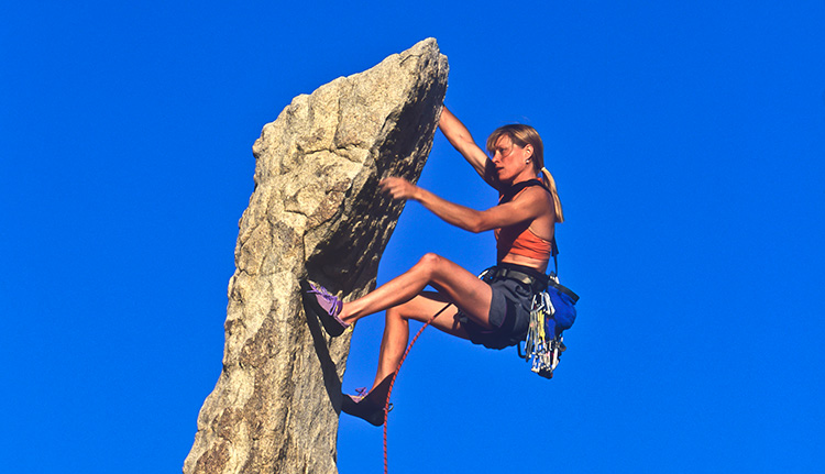 Bergsteigerin in der Felswand vor blauem Himmel